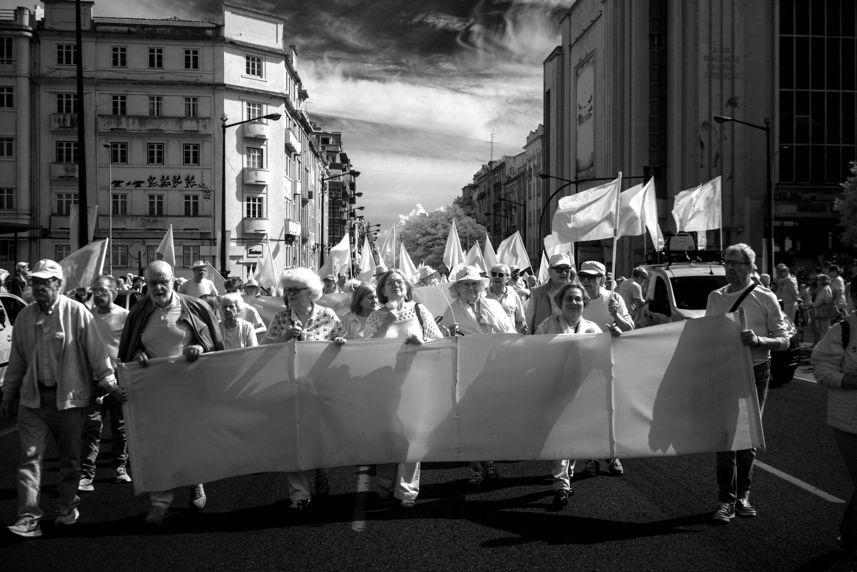 A group of protestors walk with empty signs and flags during a demonstration in Lisbon. The infrared camera cannot see the printed images, so they appear empty.